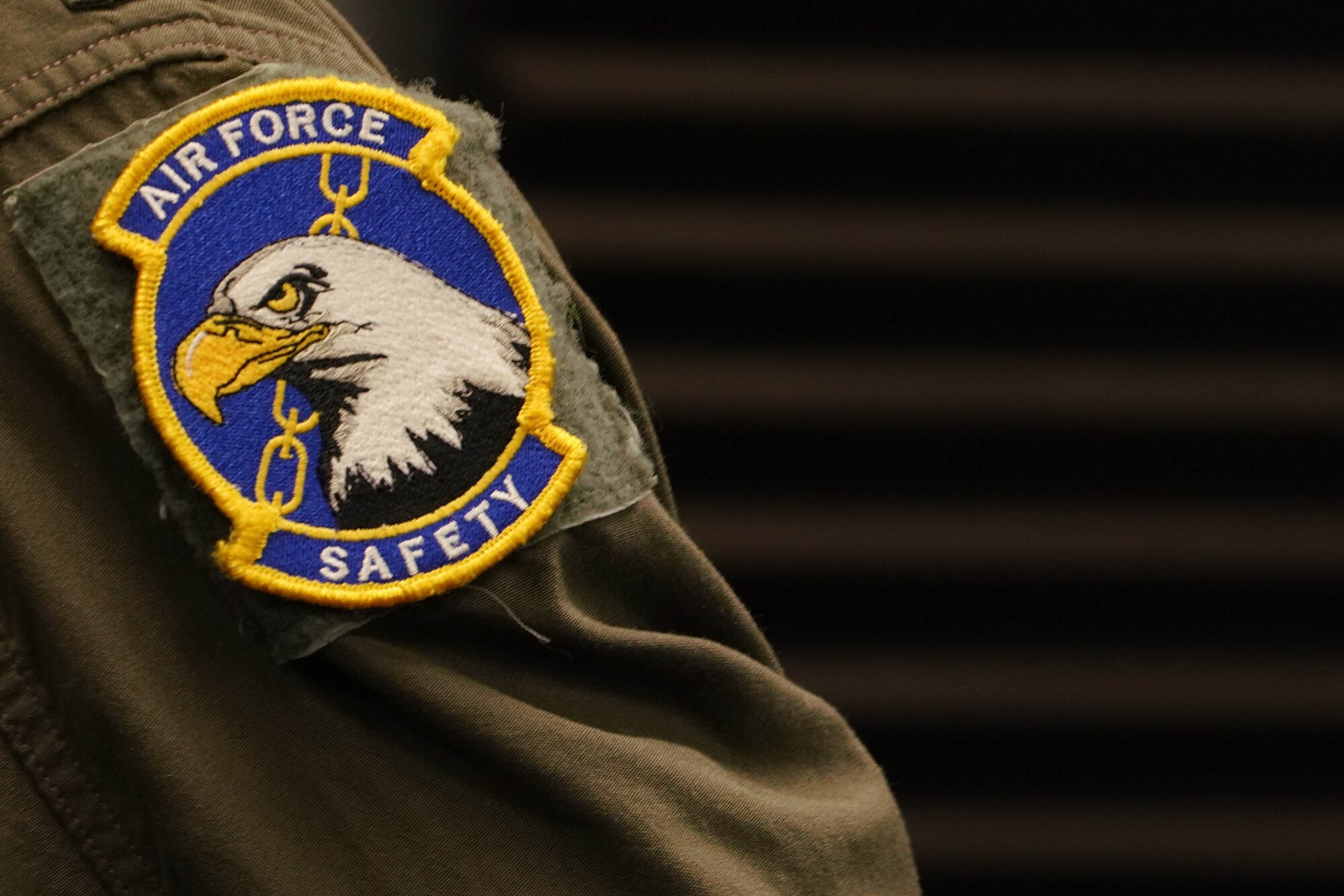 A round patch displaying an eagle, a chain link and the text "air Force Safety" attached to a flight suit sleeve.
