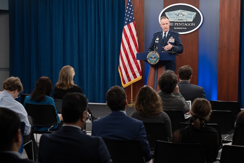 An airman at a lectern speaks to a seated audience.