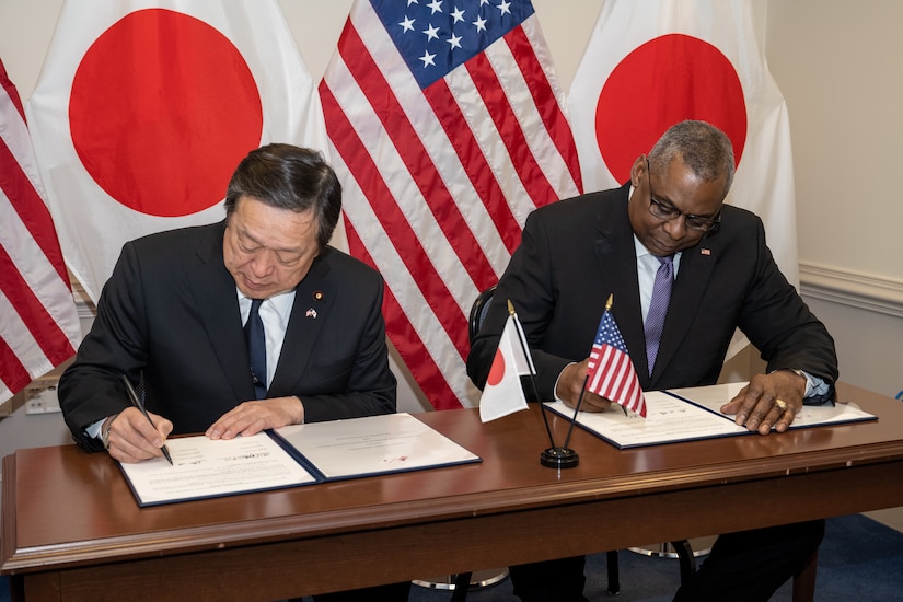Two men sign documents at a table.