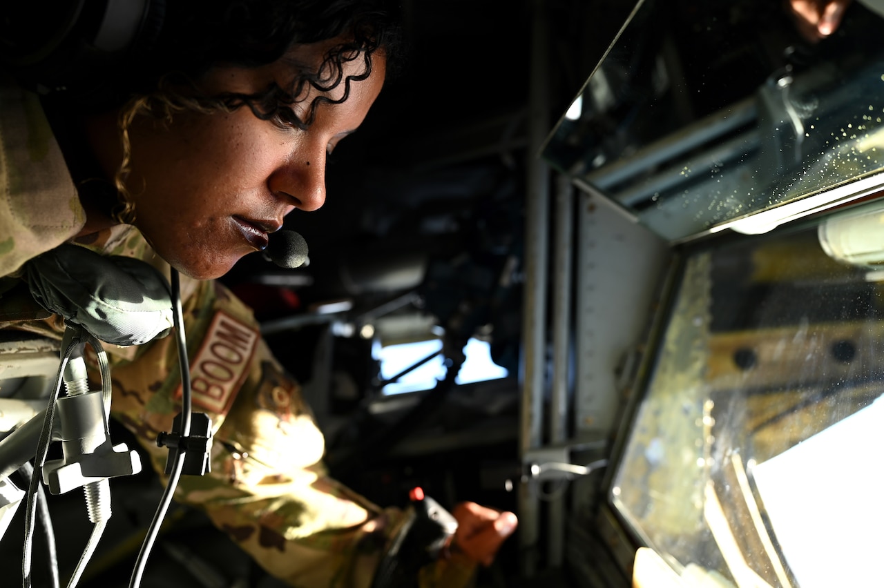 An airman looks out below from an enclosed space inside of an aircraft.