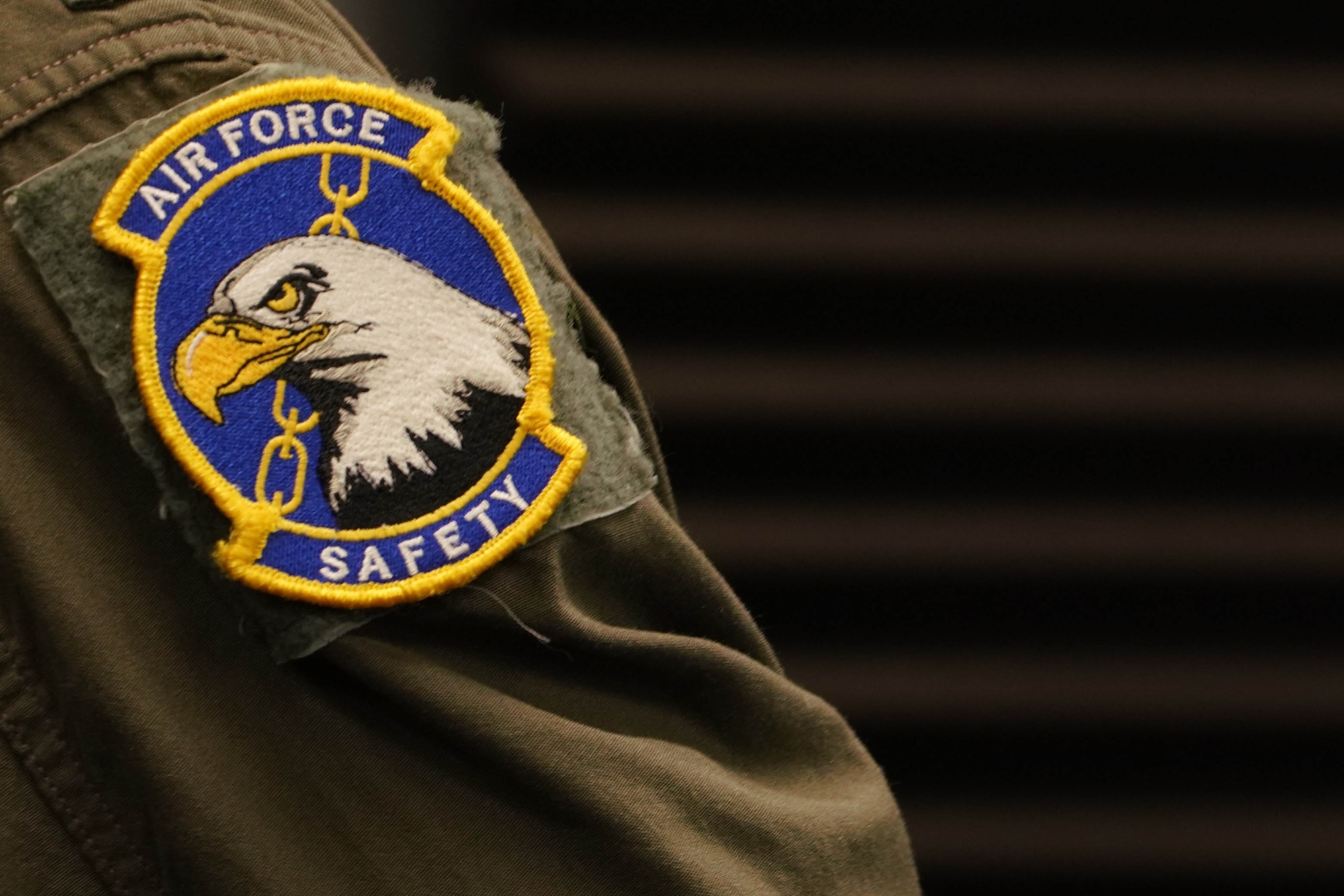 A round patch displaying an eagle, a chain link and the text "air Force Safety" attached to a flight suit sleeve.