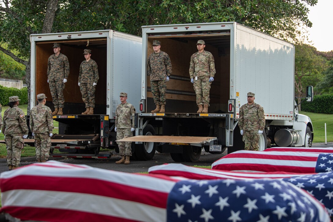 Service members stand at attention near flag-draped caskets.