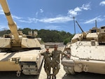 Texas National Guard members Staff Sgt. Elizabeth Cox, left, an M1 Abrams master gunner, and her significant other, Sgt. 1st Class Josh Simmons, a Bradley Fighting Vehicle master gunner, next to their respective armor vehicles. Cox recently became the first female in the Army National Guard to graduate from the Abrams Master Gunner school, an advanced gunnery and maintenance school that earns graduates the designation of Abrams Master Gunner.