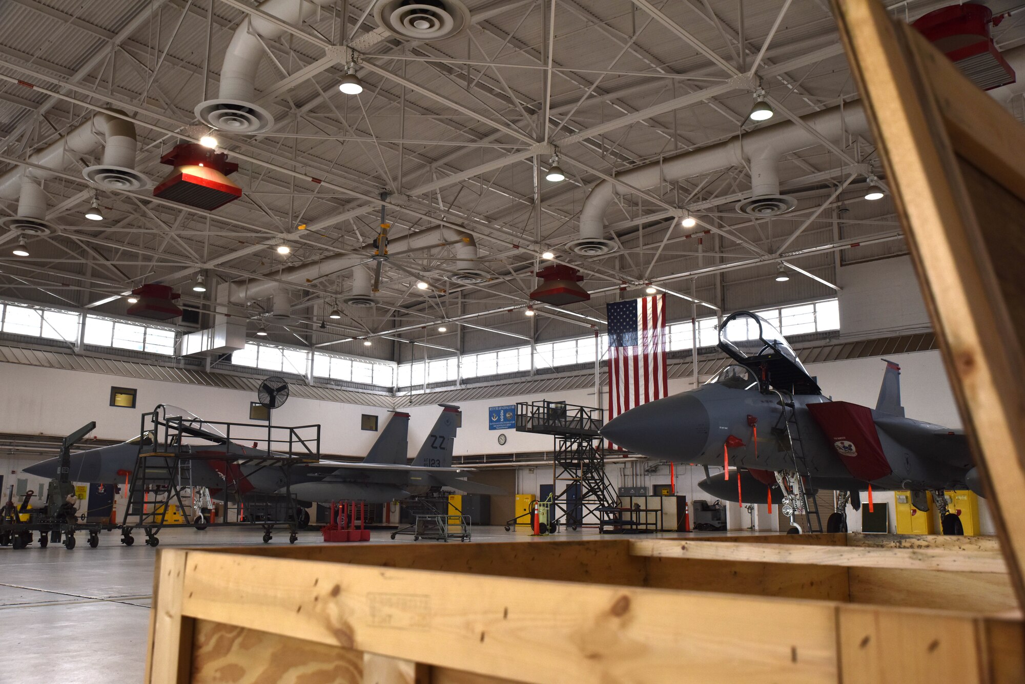 Two fighter jets sit in an aircraft hanger behind a box