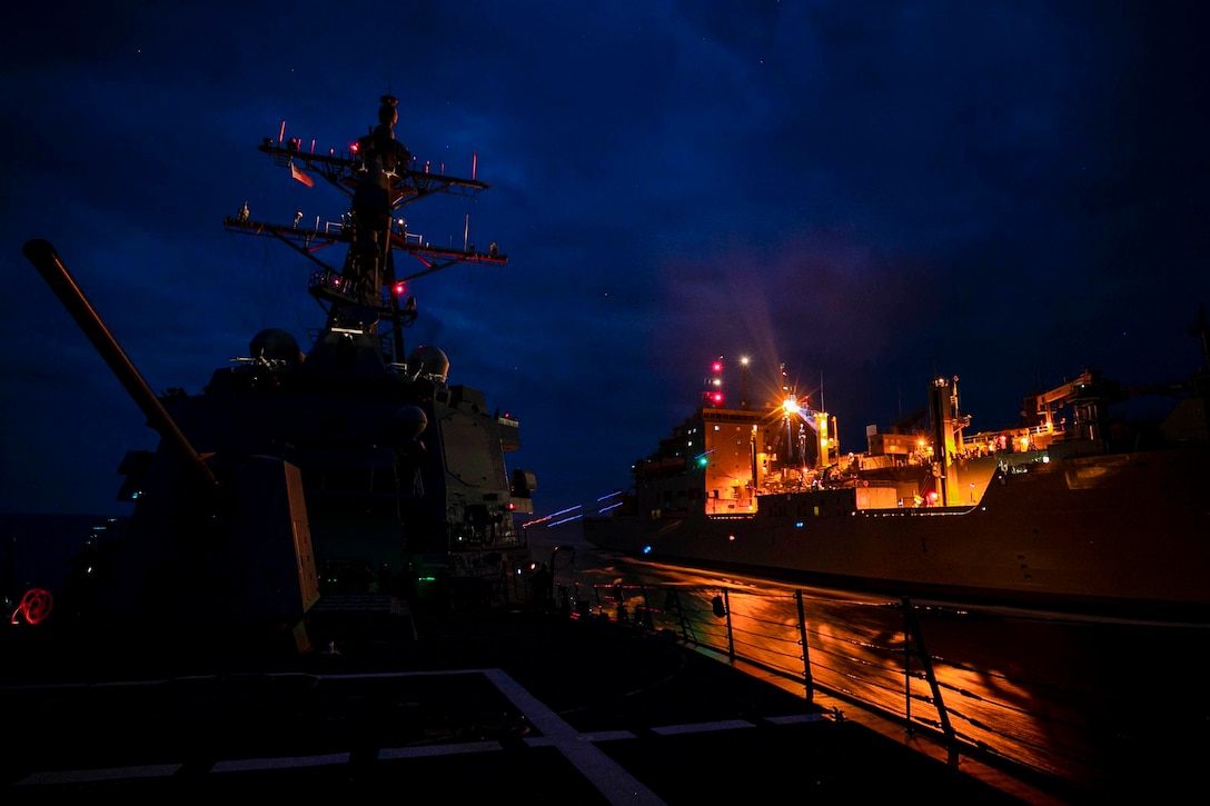 Two ships sail side by side at night.