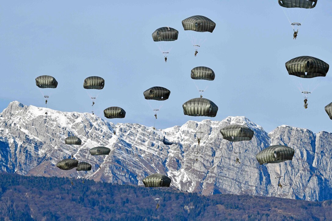 Soldiers descend in the sky wearing parachutes.