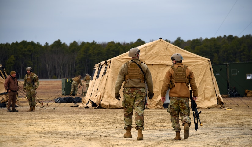 Airmen, equipped with vests and mock weapons, walk towards the tactical operations center in preparation for the Jersey Devil 23 exercise.