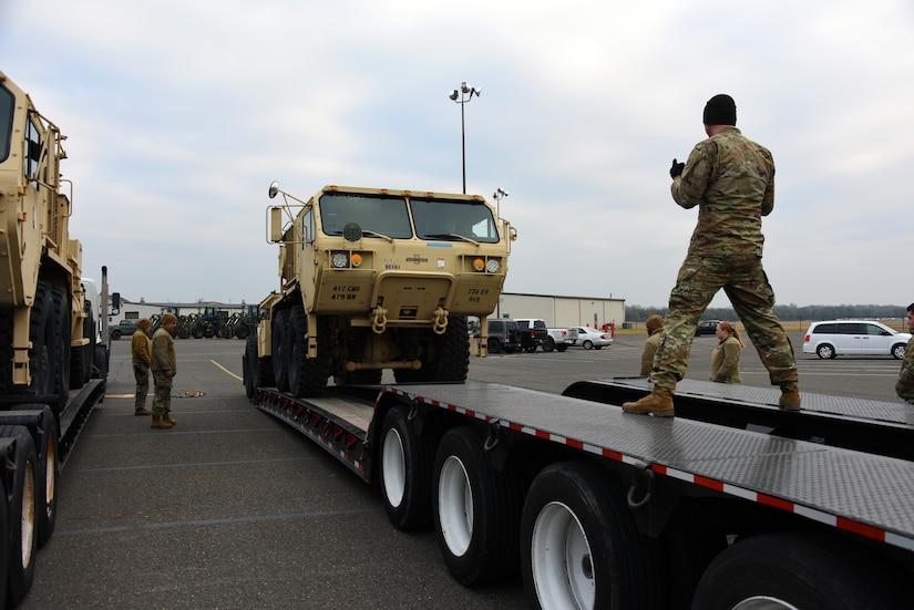 U.S. Army soldier helps driver with the onloading of a light equipment transporter.