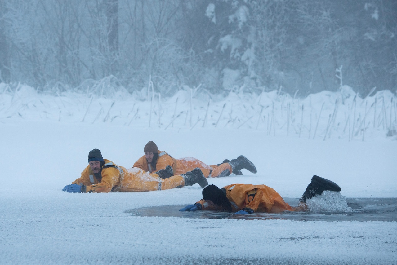 One firefighter lies in an icy puddle as two others lie on snow nearby.