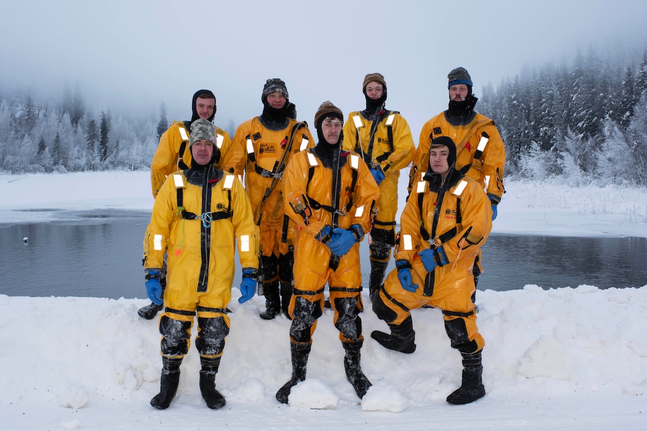 Seven firefighters in yellow dry suits stand for a photo in snow.