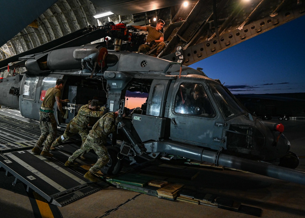 A photo of a helicopter being unloaded from a plane by people in military uniforms.