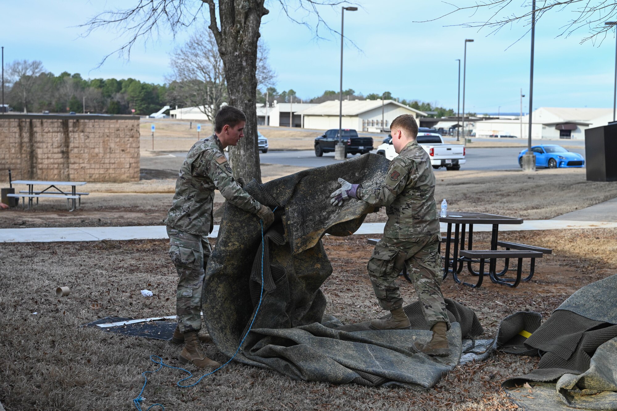 Men in uniform fold a carpet.