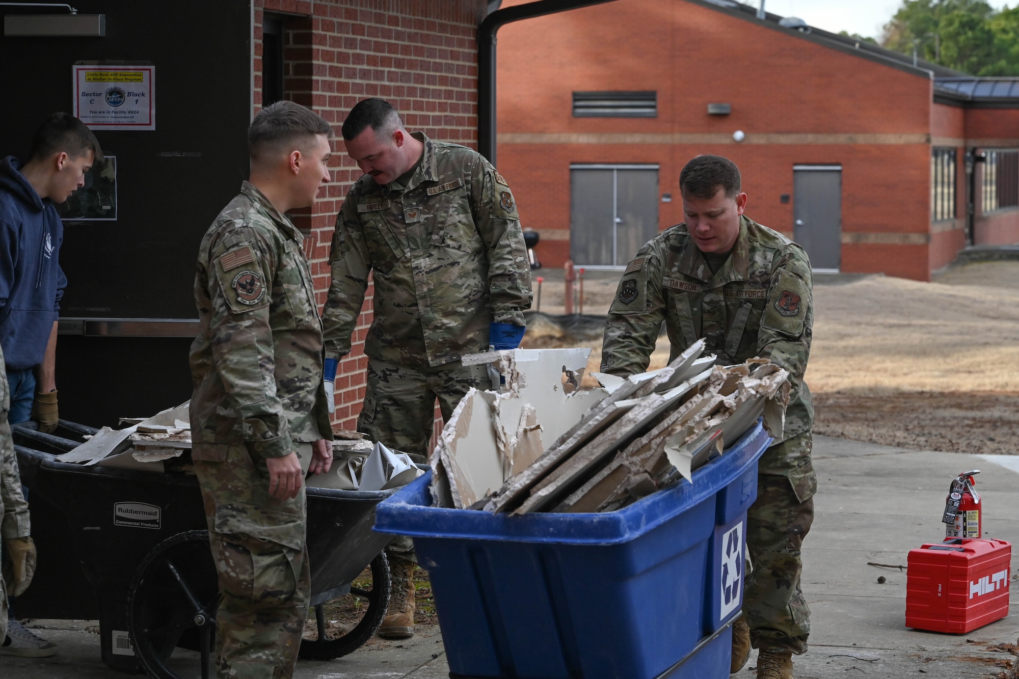 Men in uniform put drywall in a garbage bin.