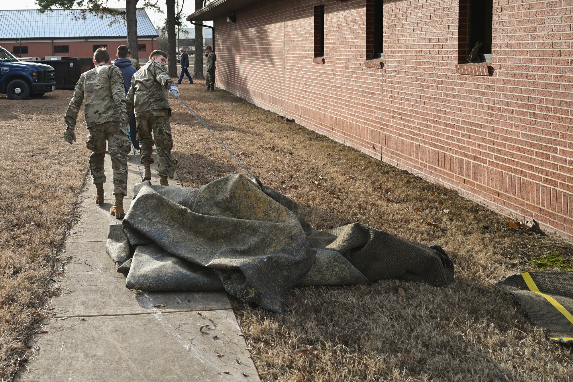 Men in uniform drag a carpet.