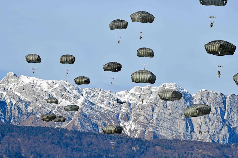 Soldiers descend in the sky wearing parachutes.