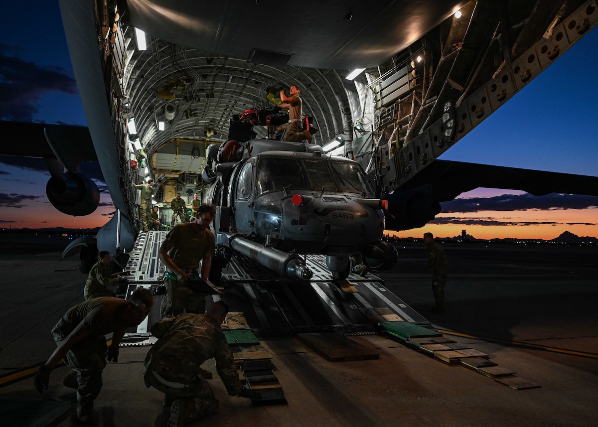 A photo of a helicopter being unloaded from a plane by people in military uniforms.