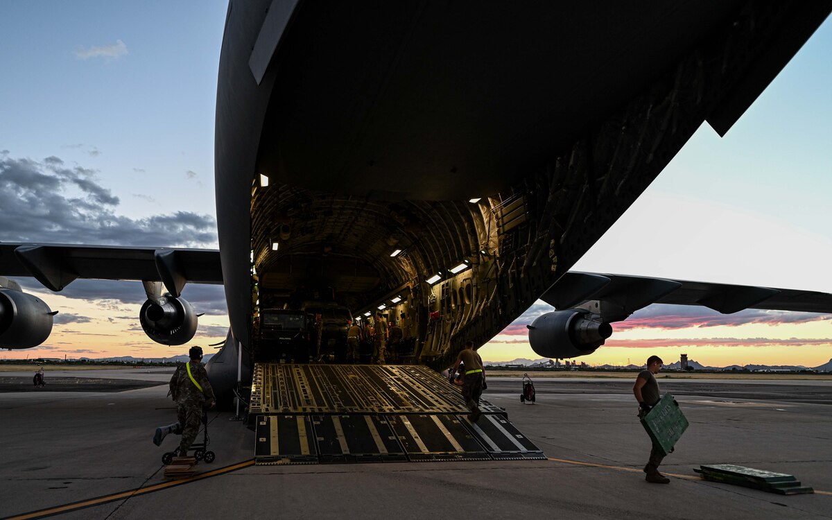 A photo of a helicopter being unloaded from a plane by people in military uniforms.