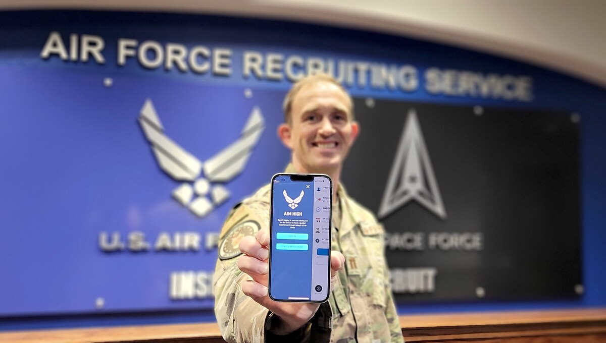 Air Force captain poses with his phone showing the Aim High mobile application screen
