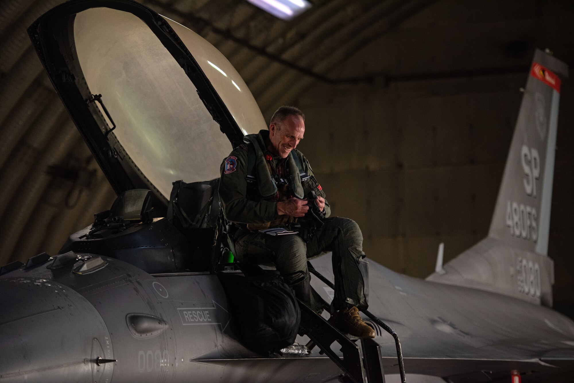 A pilot sitting in an F-16 smiles as he talks to a crew chief below.