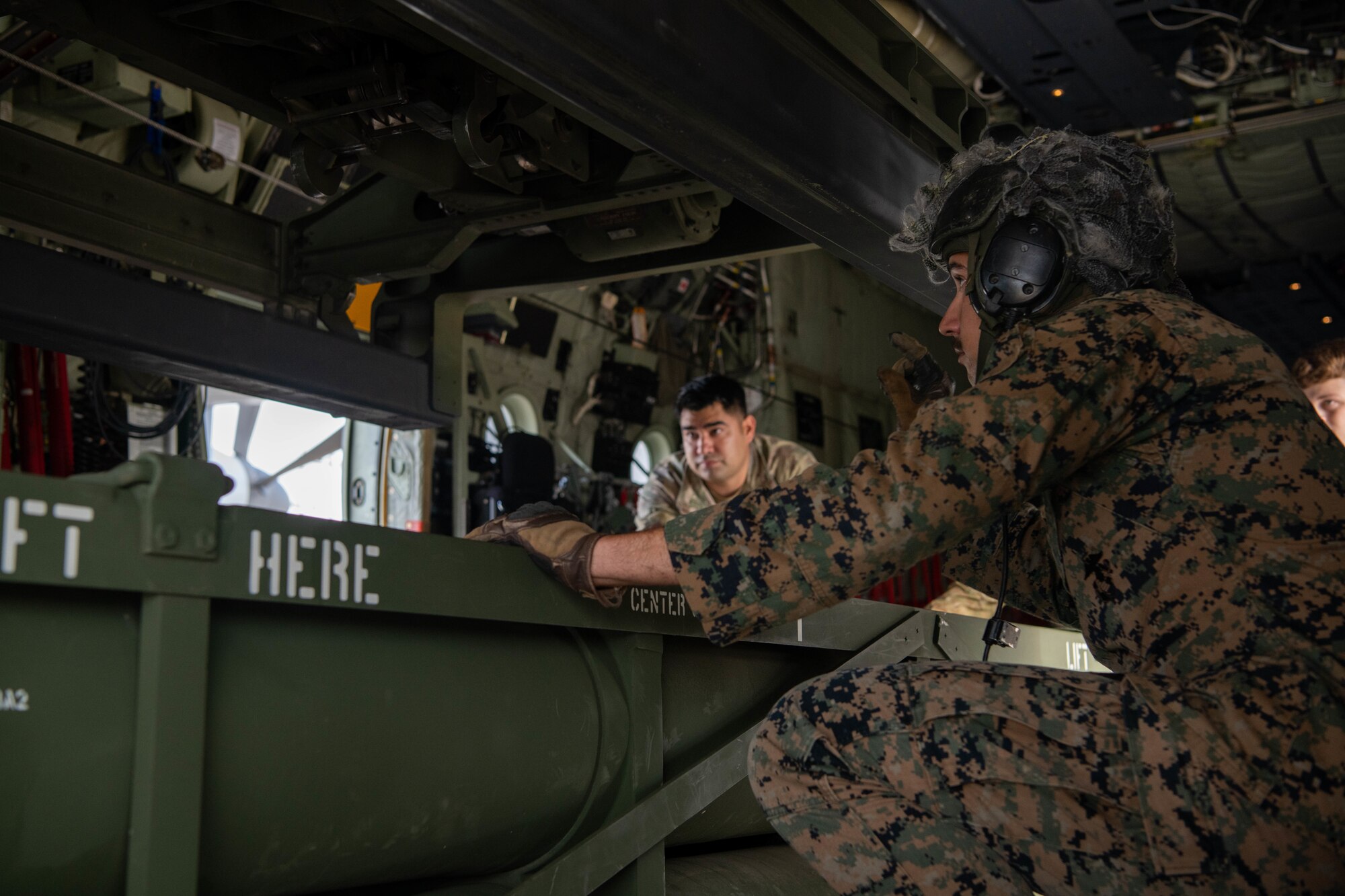 Airmen and Marines load an ammo pod into an aircraft.