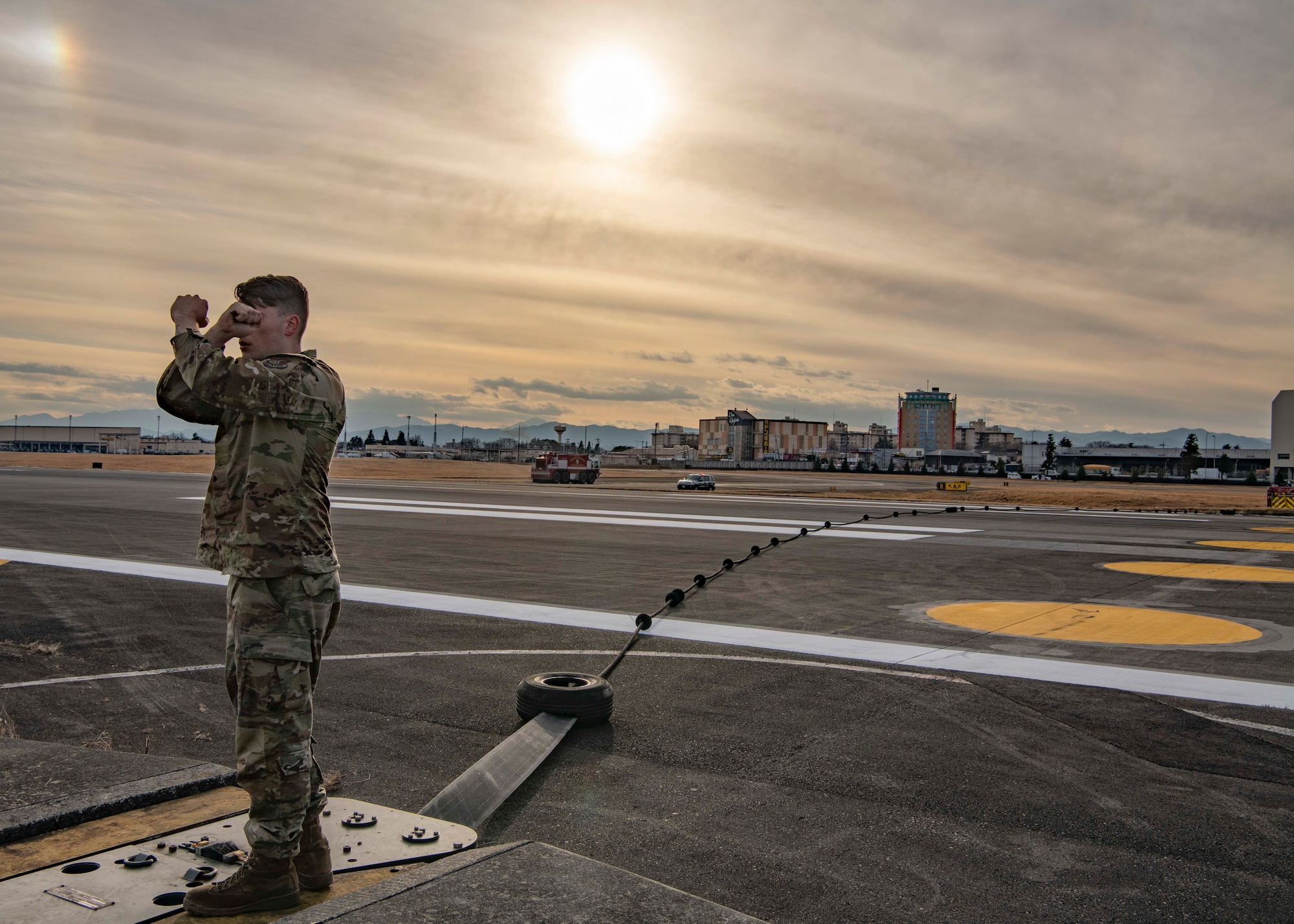 Senior Airman Jacob Handler, 374th Civil Engineer Squadron power production journeyman, gives hand signals to Aircraft Arresting System (AAS) operators after the completion of an annual certification test at Yokota Air Base, Japan, Jan 6, 2023.