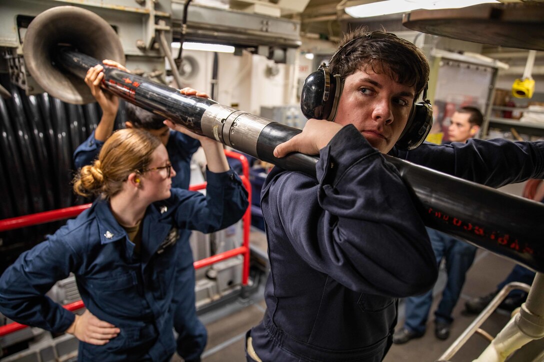 Sailors hold up a cable on a ship.