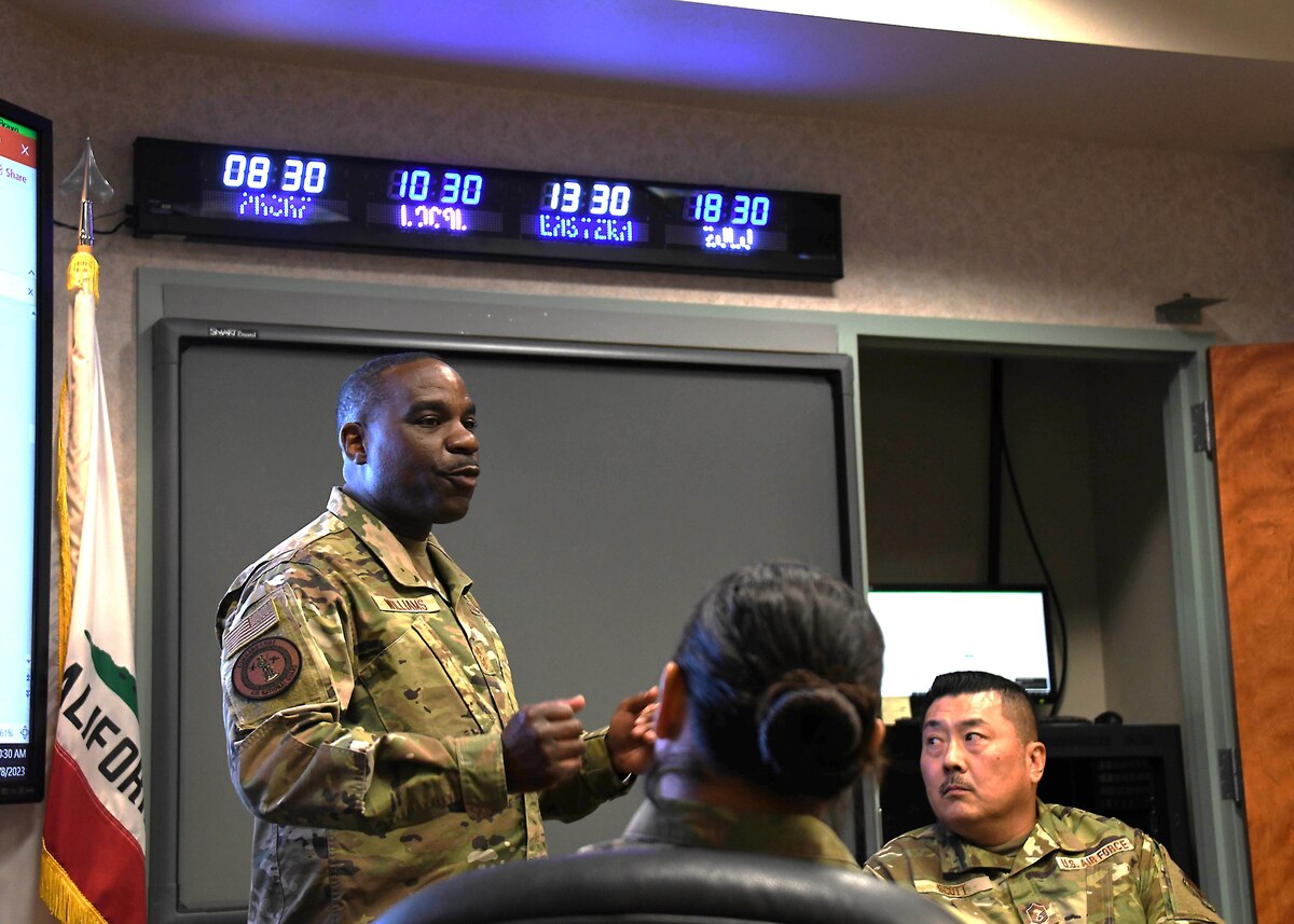 A man in a camouflage uniform speaks in a room
