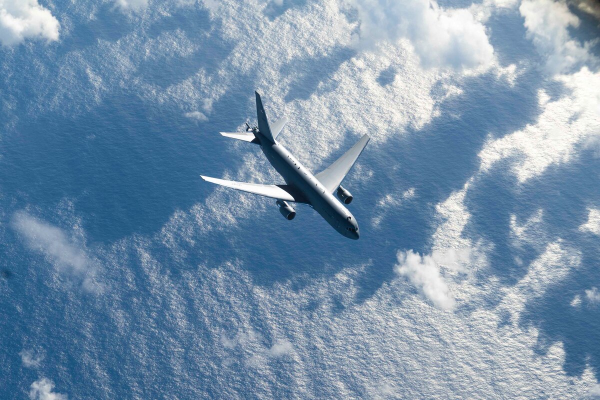 An aircraft flies over water and clouds.