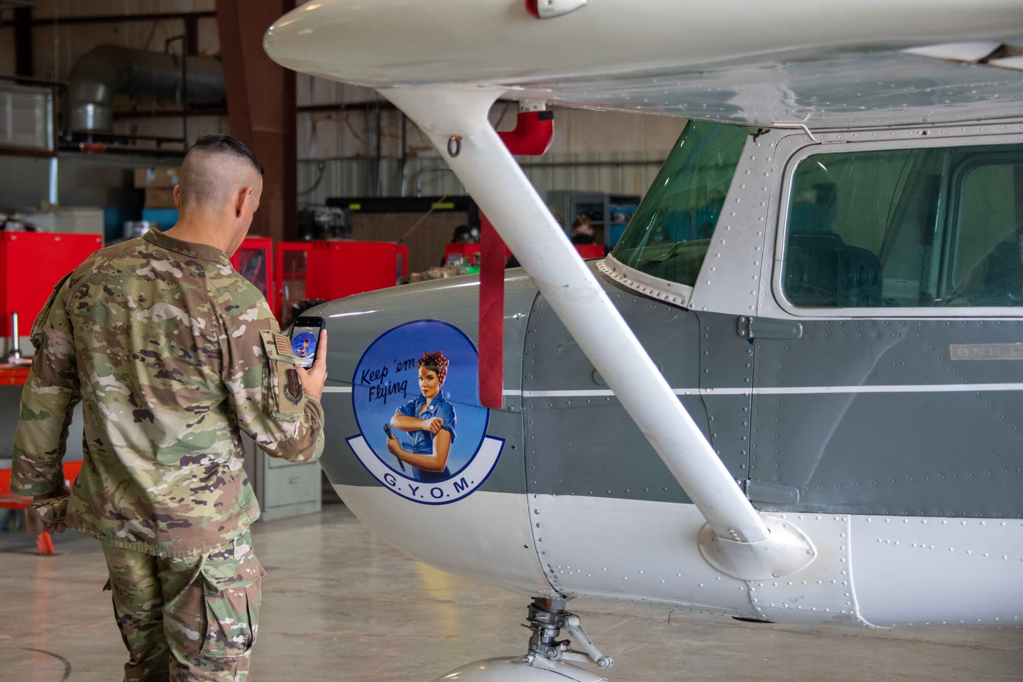 Chief Master Sgt. Cesar Flores, 97th Air Mobility Wing command chief, snaps a picture of the “Grow Your Own Mechanic” logo displayed on a plane in Hangar 33 in Altus, Oklahoma, Jan.11, 2023. The plane was designed and built by students from the Southwest Technology Center within the GYOM program. (U.S. Air Force photo by Airman 1st Class Kari Degraffenreed)