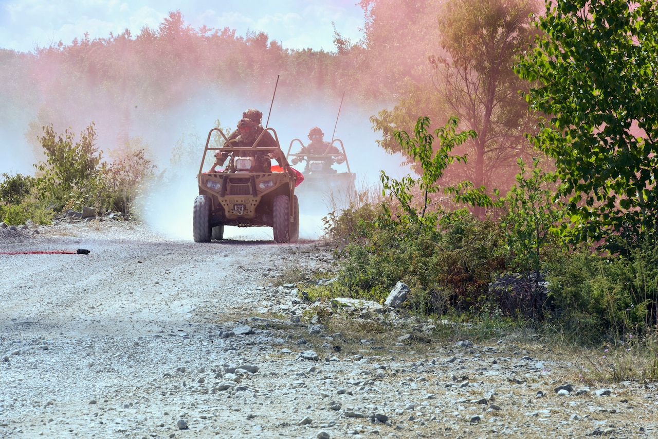 Soldiers ride in tactical vehicles on a dirt road.