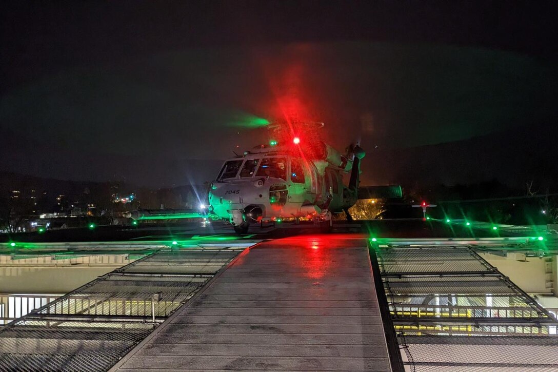 A helicopter illuminated by red and green lights sits in a makeshift landing zone at night.