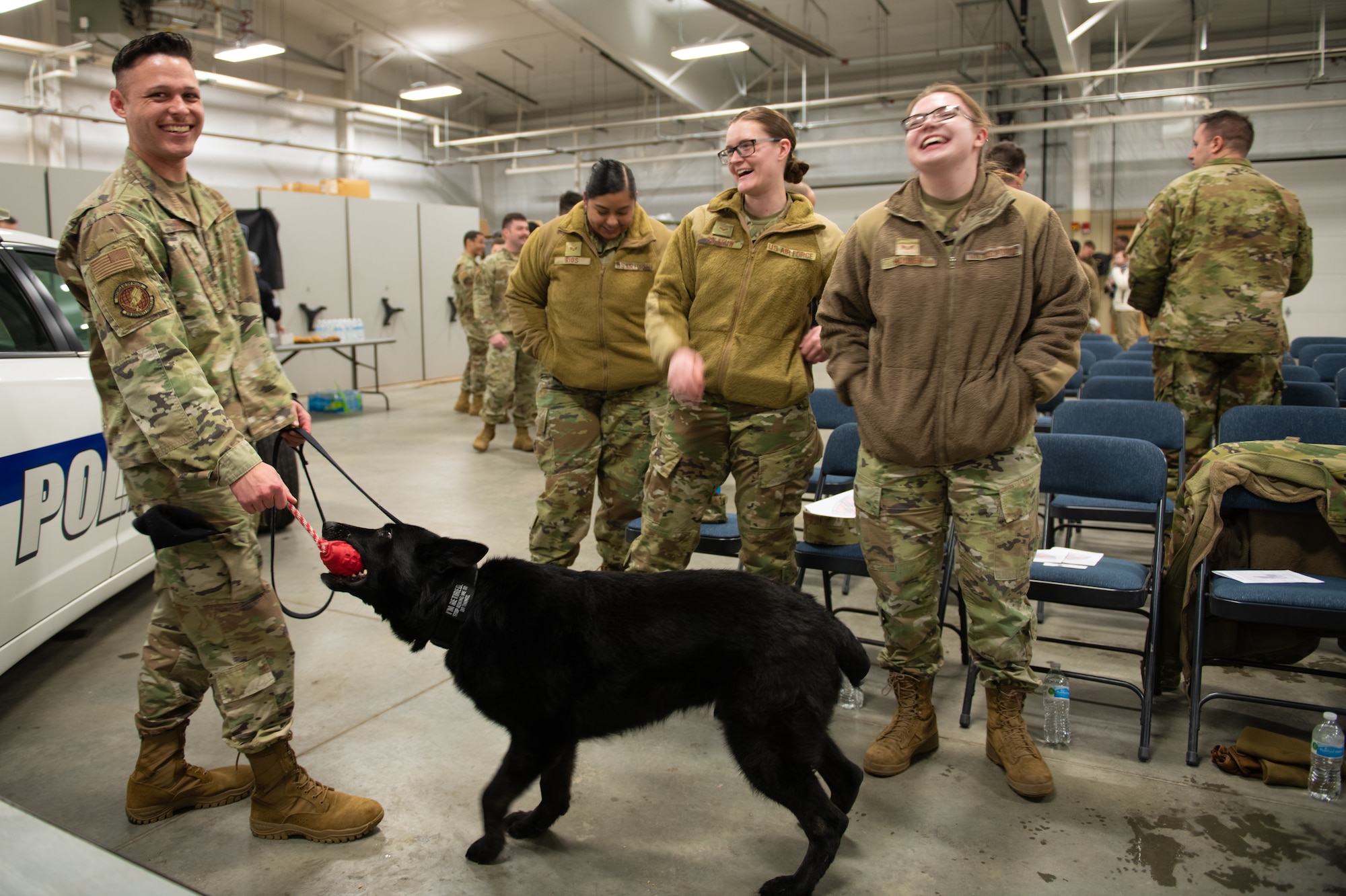 A man in a green uniform plays with black dog.