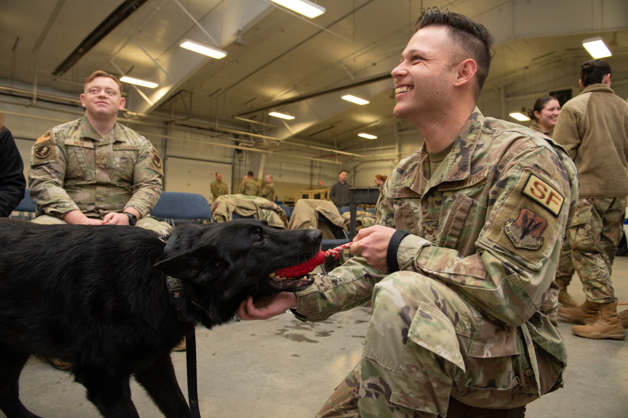 A man in a green uniform plays with a black dog.