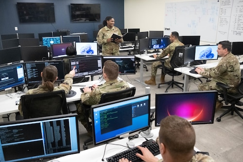 Capt. Ashley Oates, 275th Cyberspace Operations Squadron flight commander, center standing, briefs Airmen assigned to the 275th COS at Warfield Air National Guard Base at Martin State Airport, Middle River, Md., Jan. 10, 2023. Oates led a cyber protection team that was the first team in the Air National Guard to certify on a live Department of Defense network. (U.S. Air National Guard photo by Master Sgt. Chris Schepers)