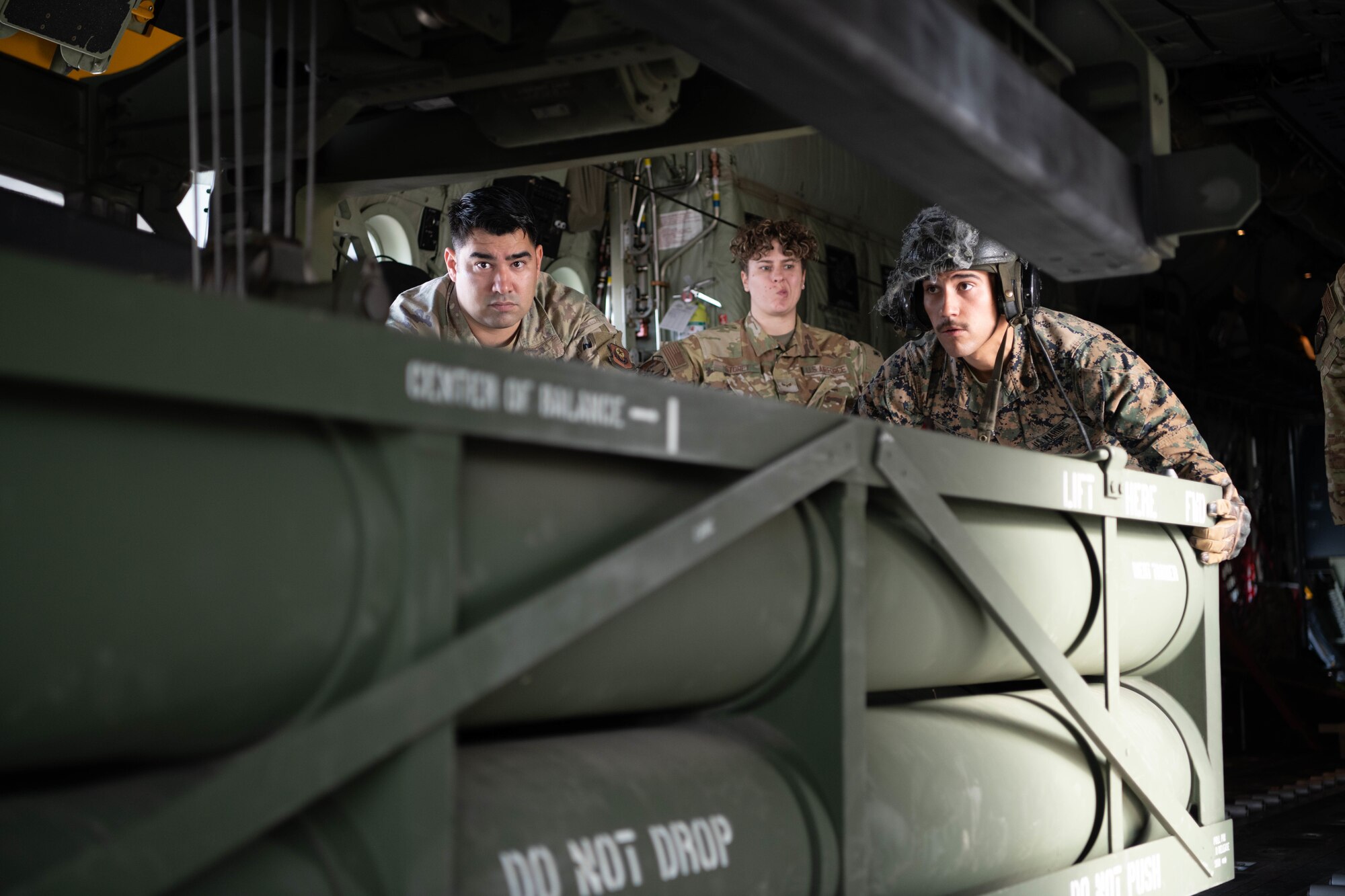 A Marine and Airmen load an ammo pod into an aircraft.
