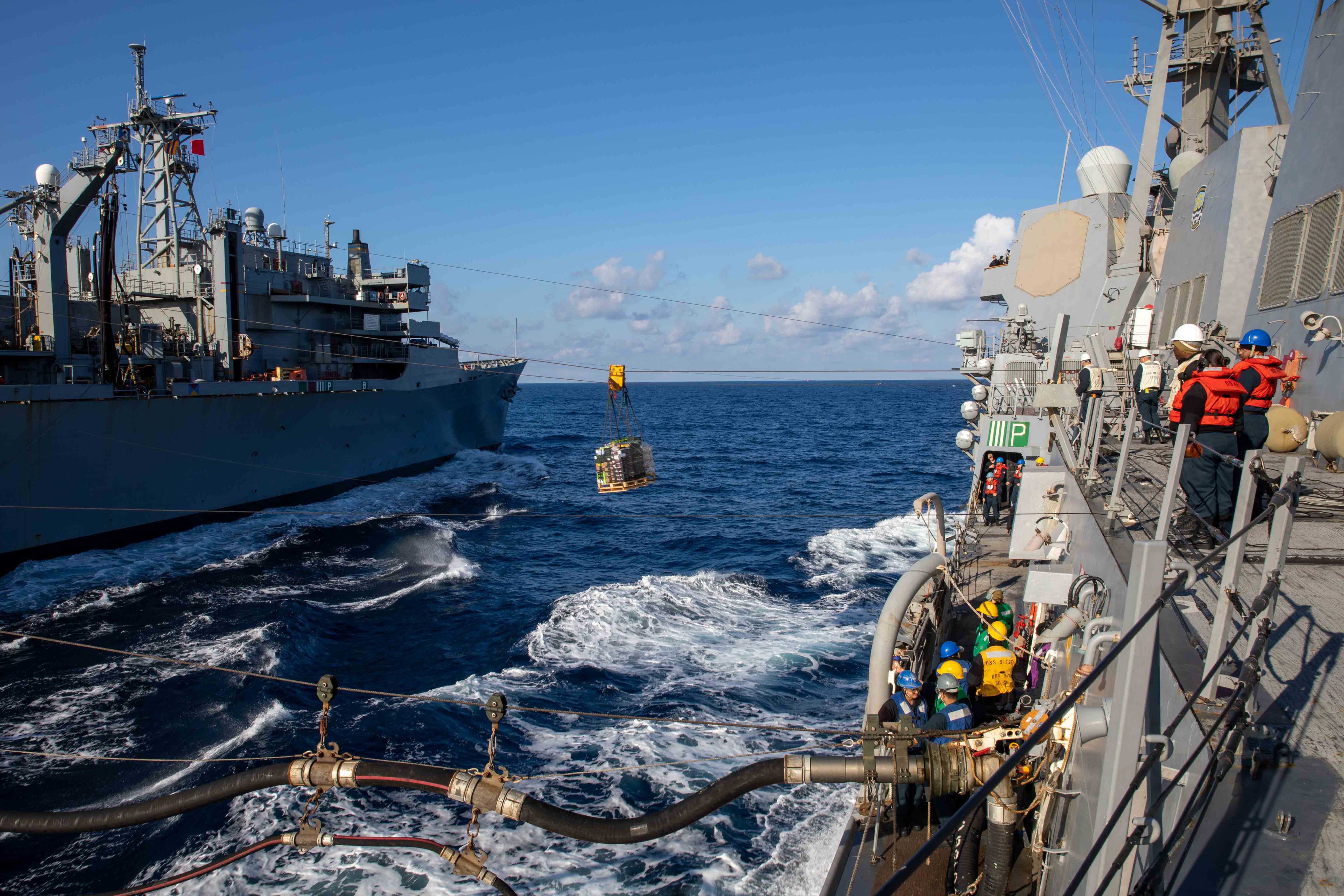 Two Navy ships are shown parallel at sea during a supply replenishment.