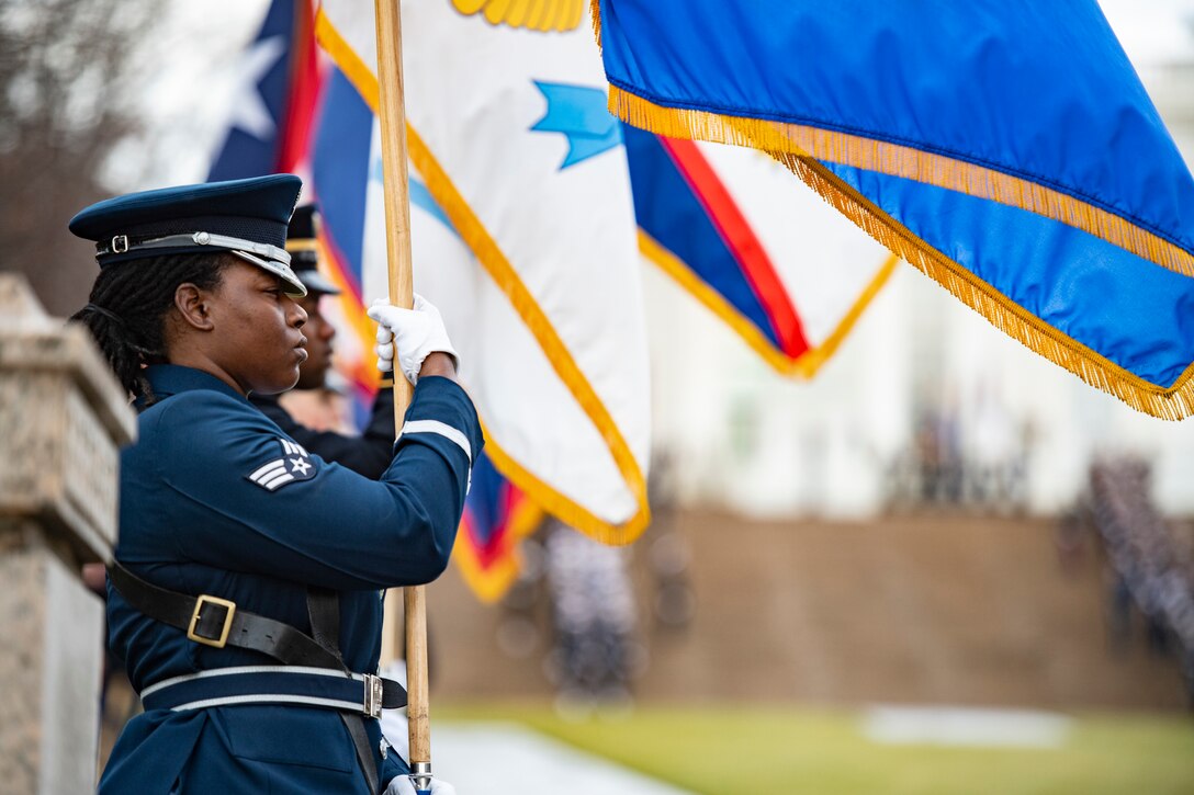 Service members in formal uniforms hold flags and stand at attention.