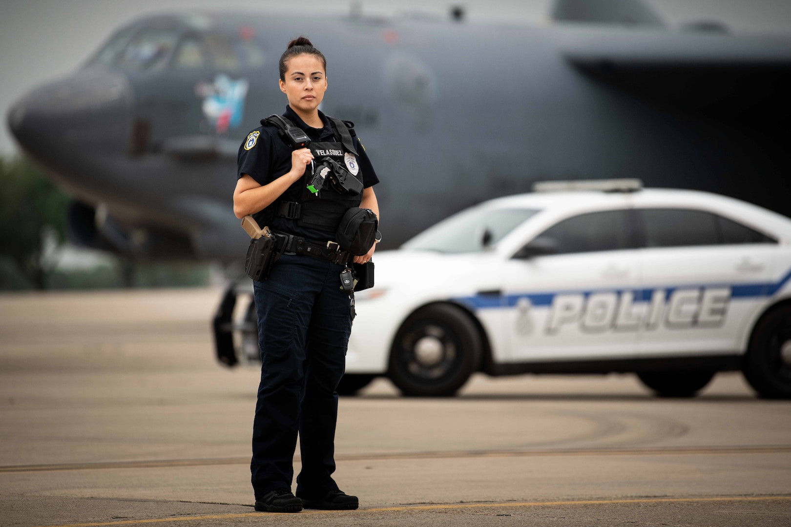 female law enforcement officer stands in front of a vehicle and a plane