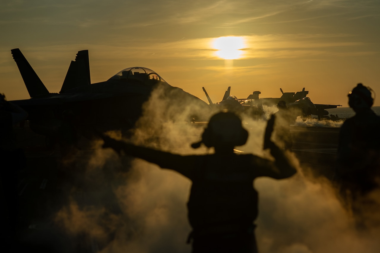 A sailor directs a military aircraft on the flight deck of the USS Nimitz while at sea.