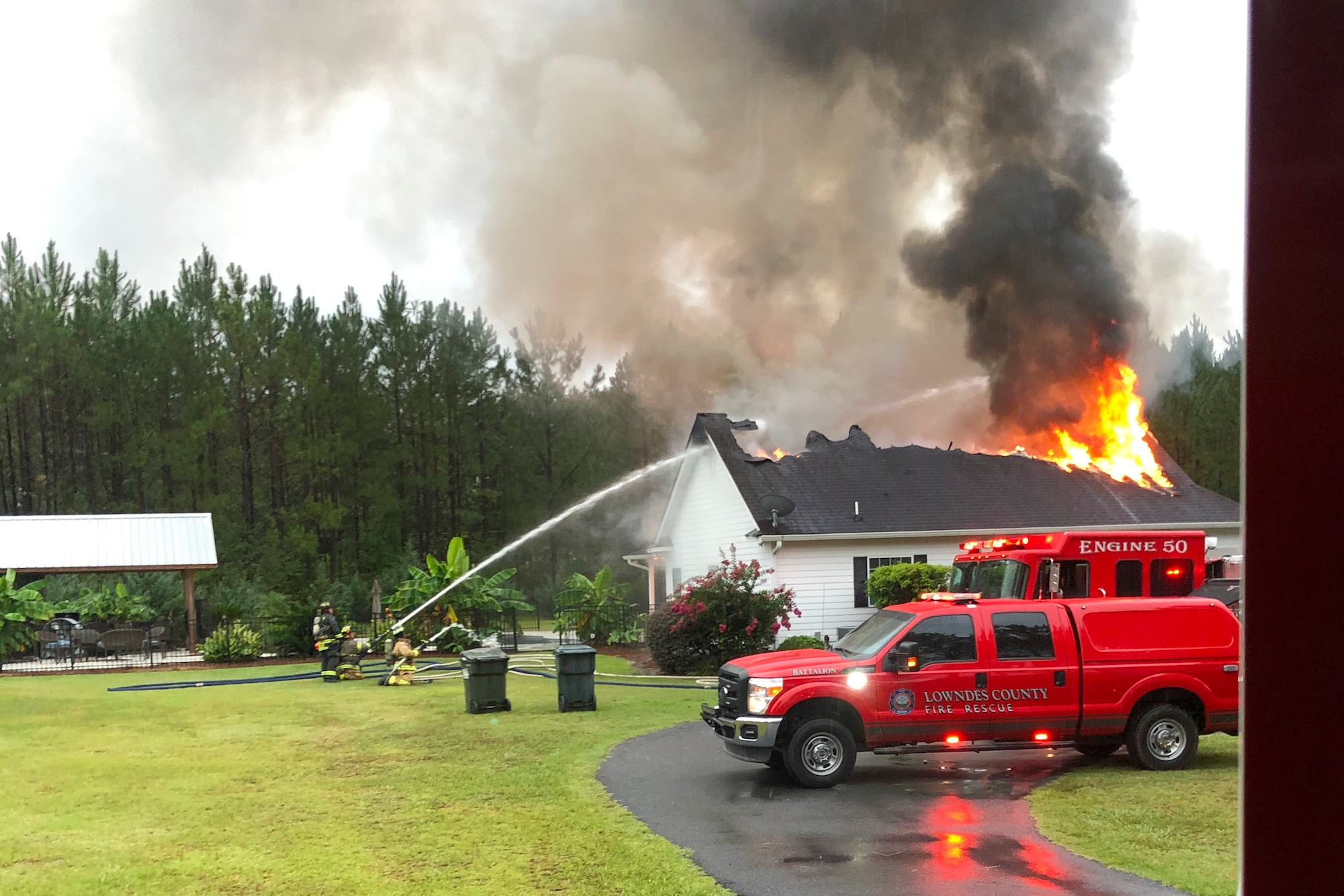 A photo of a fire truck and firemen putting out a fire on a burning house.