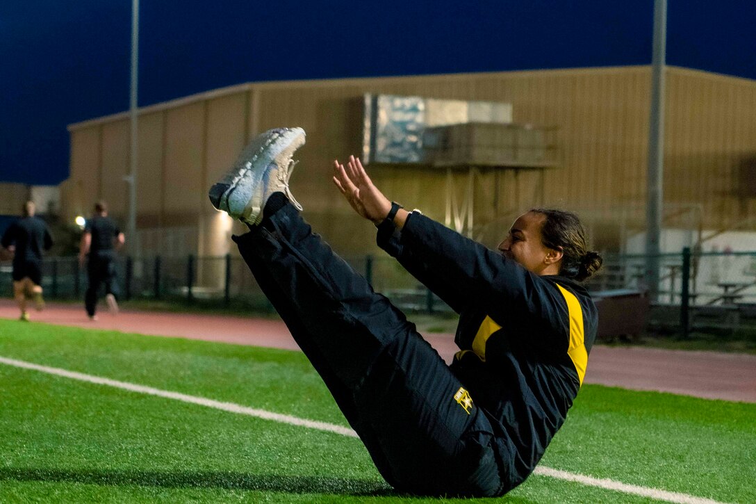 A soldier does a v-up core exercise on grass at night.