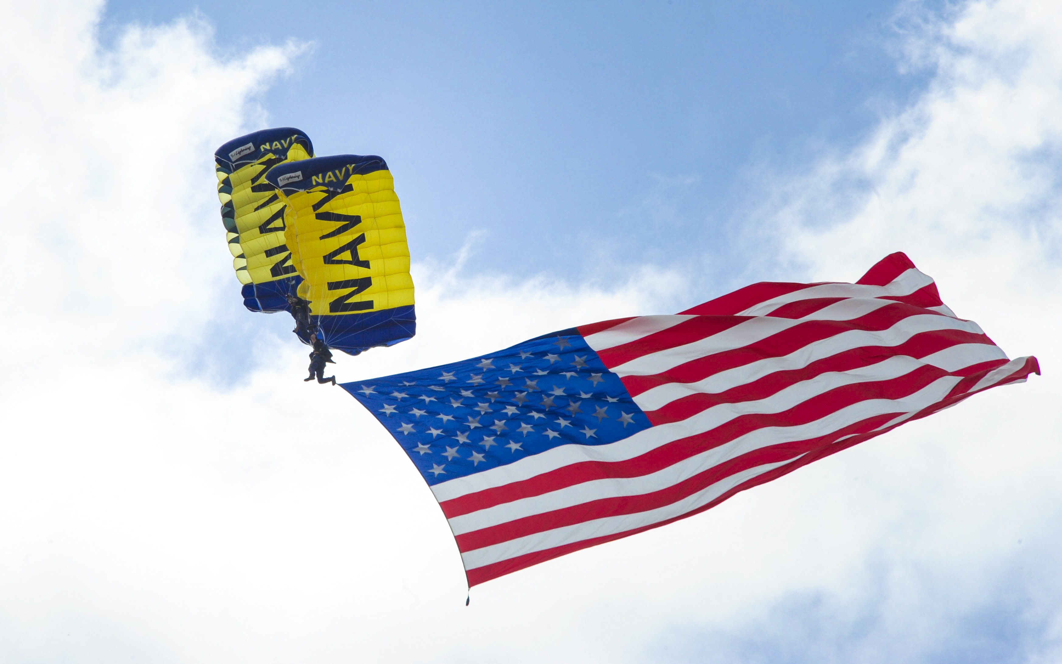 Parachute Rigger 1st Class Victor Maldonado (bottom) and Special Warfare Operator 1st Class T.J. Amdahl, members of the Navy Parachute Team, the Leap Frogs, fly the American flag as they perform a biplane maneuver above the Circuit of The Americas racetrack at the Summer X Games