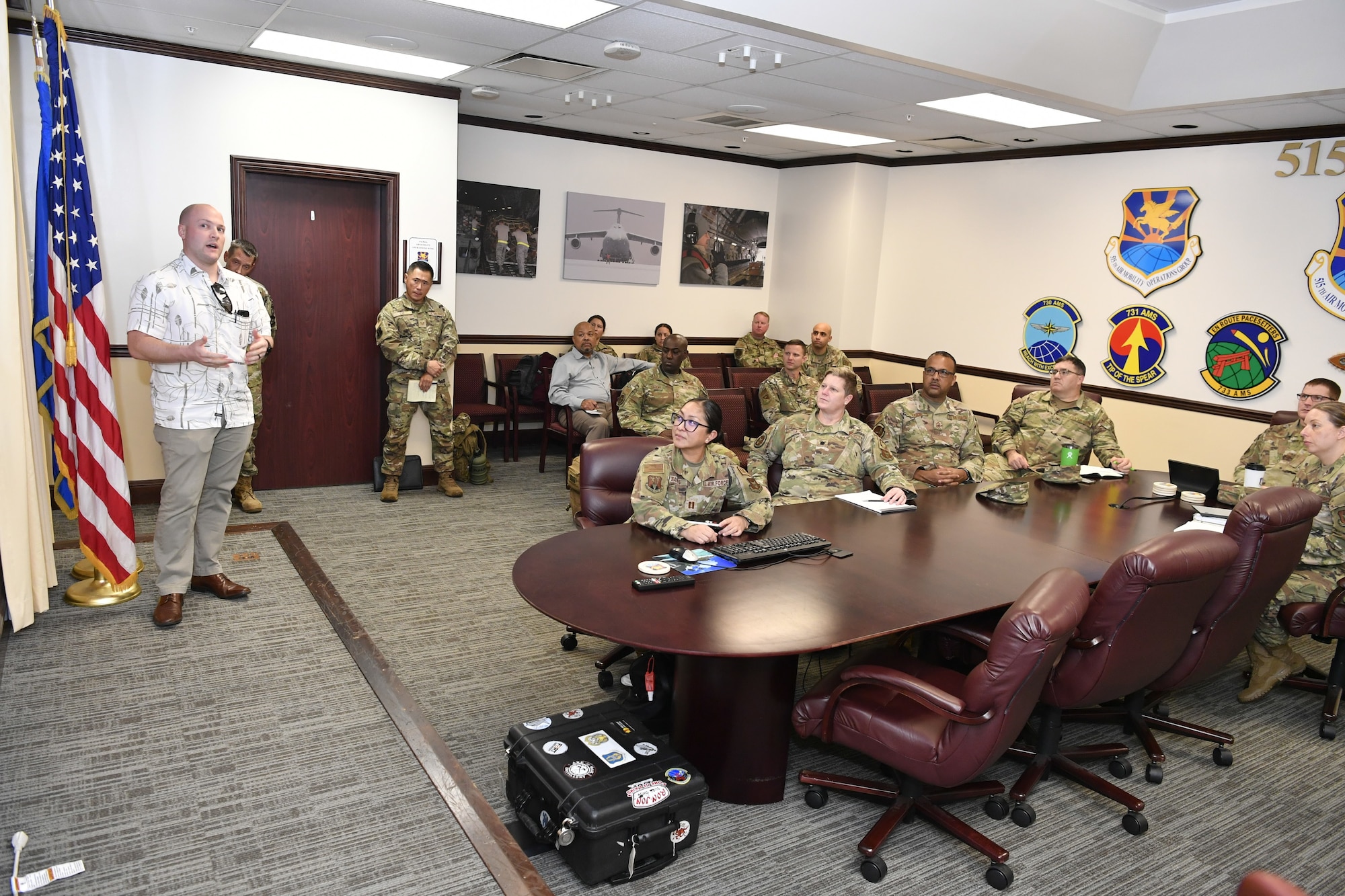 Civilian and military members sit around conference table as presenter briefs all.