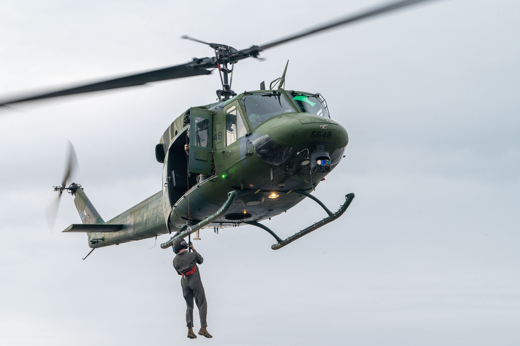 A U.S. Air Force Senior Airman Devin Hackney, 36th Rescue Squadron special mission aviator, hoists down from a UH-1N Huey as a demo prior to the celebration of UH-1N Huey number 6648 reaching 20,000 flight hours at Fairchild Air Force Base, Washington, Jan. 13, 2023. The Huey reaching 20,000 is the highest number of flight hours for Huey’s across the Department of Defense. (U.S. Air Force photo by Airman 1st Class Stassney Davis)