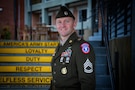 man wearing u.s. army uniform stands in front of staircase