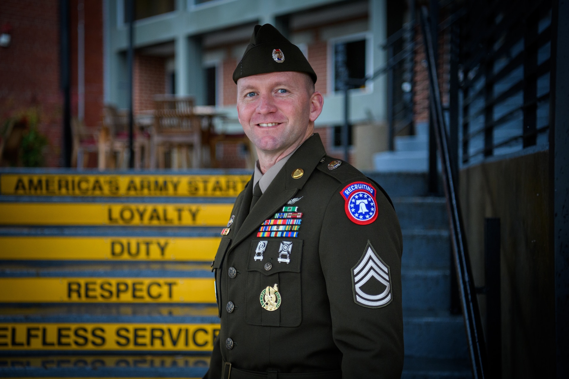man wearing u.s. army uniform stands in front of staircase