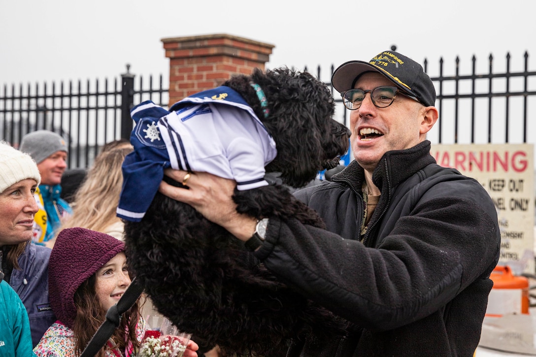 A sailor smiles as he holds a dog in his arms.