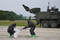 Two technicians put an unmanned aerial system into a bag for decon in front of a NBCRV.