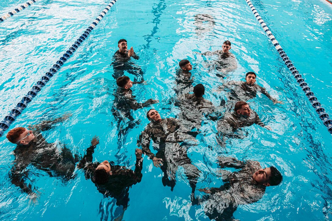 Marines wearing uniforms float in a pool.