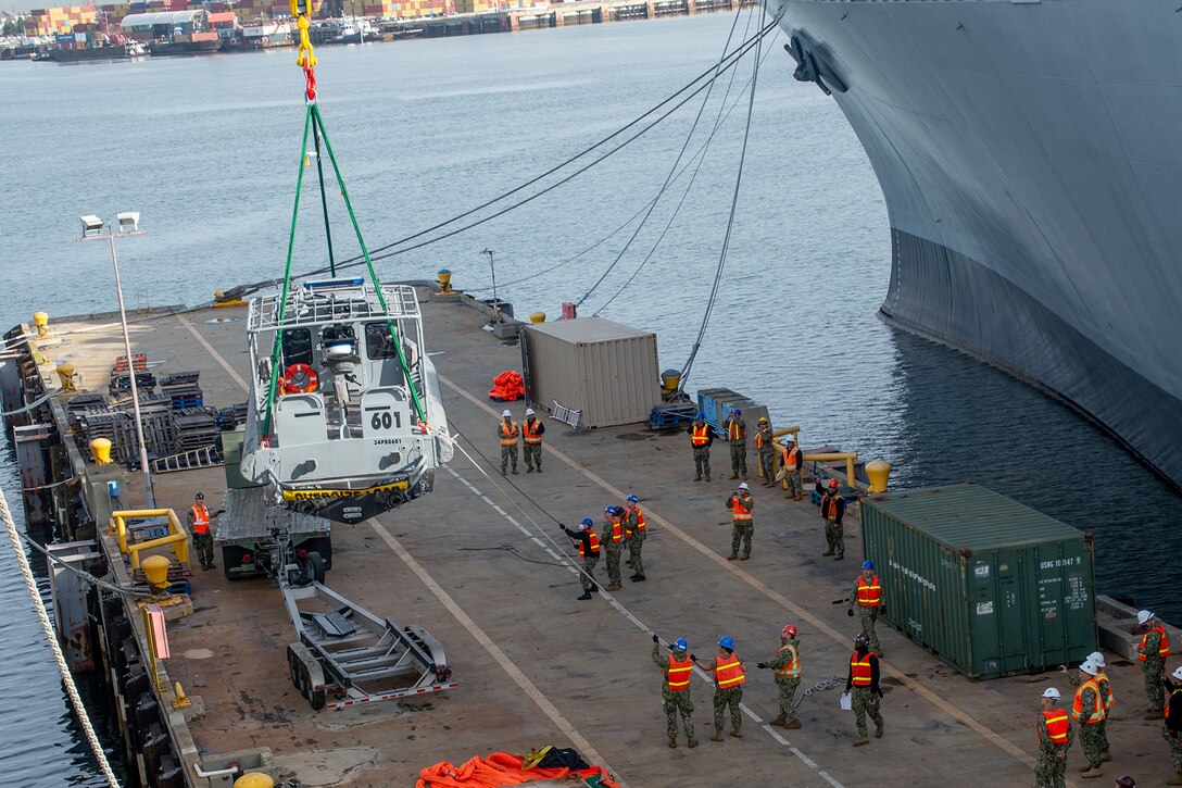 A patrol boat is raised from a loading area using ropes attached to a Navy ship.